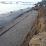 La Trocha revetment — compaction layer over geotextile tubes with bridge backdrop