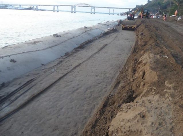 La Trocha revetment — compaction layer over geotextile tubes with bridge backdrop