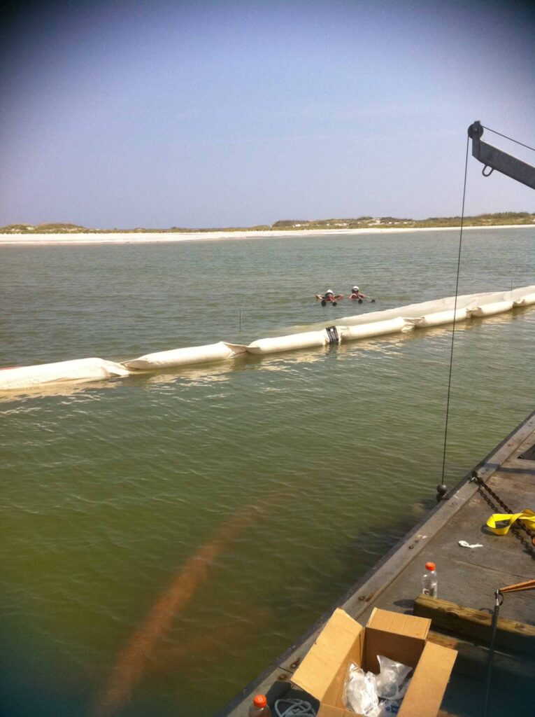 TITAN Boom™ turbidity control barrier deployment — crew positioning boom from barge in open water