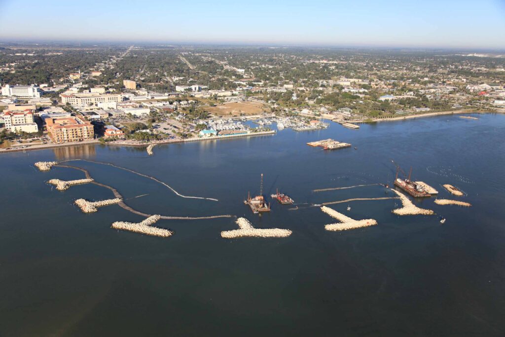 Aerial view — TITANTube® breakwater structures under construction with crane barges in coastal bay