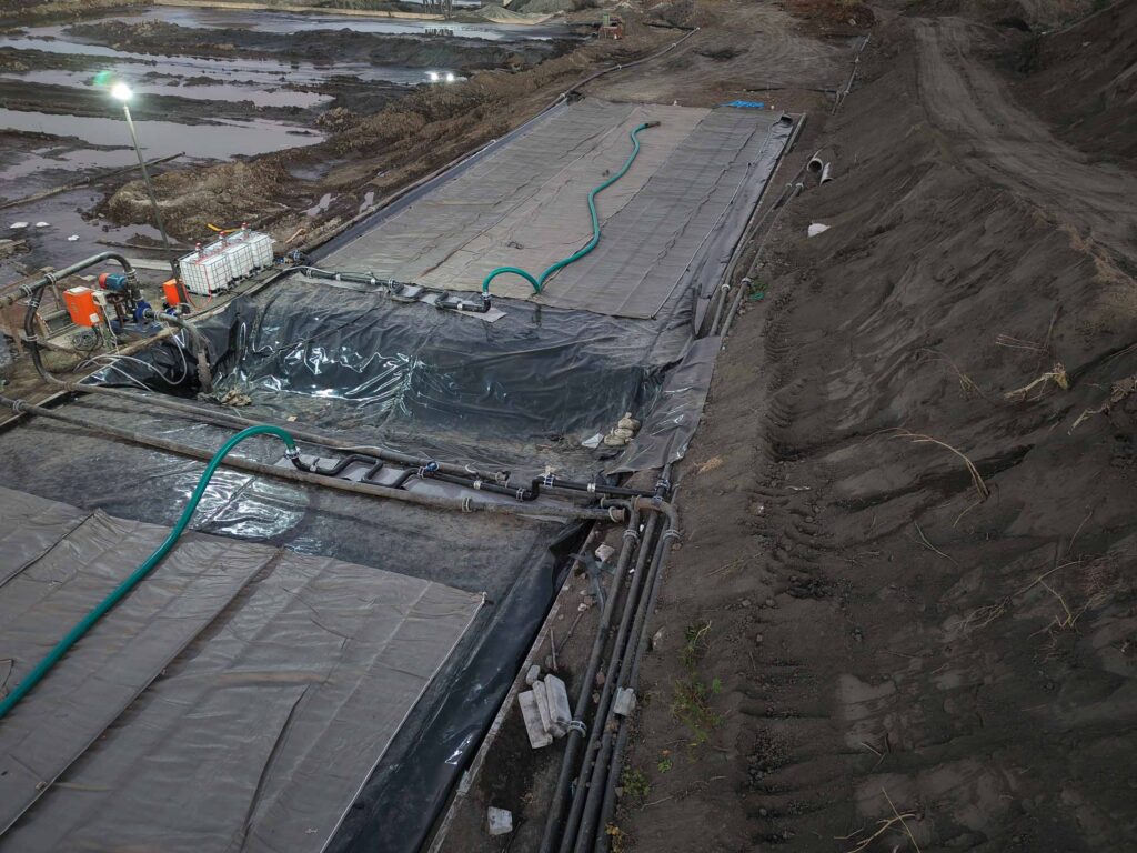 Chrome ore geotextile tube dewatering — aerial drone view of containment cells with fill hoses at night