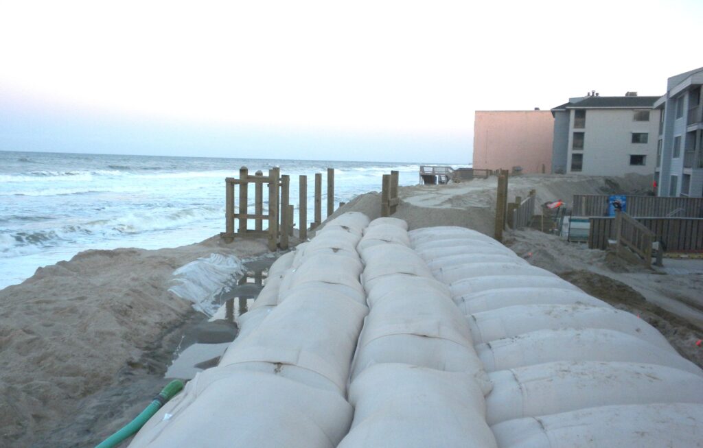 TITANBag® beachfront revetment — filled bags forming a dune-toe protection structure alongside oceanfront buildings